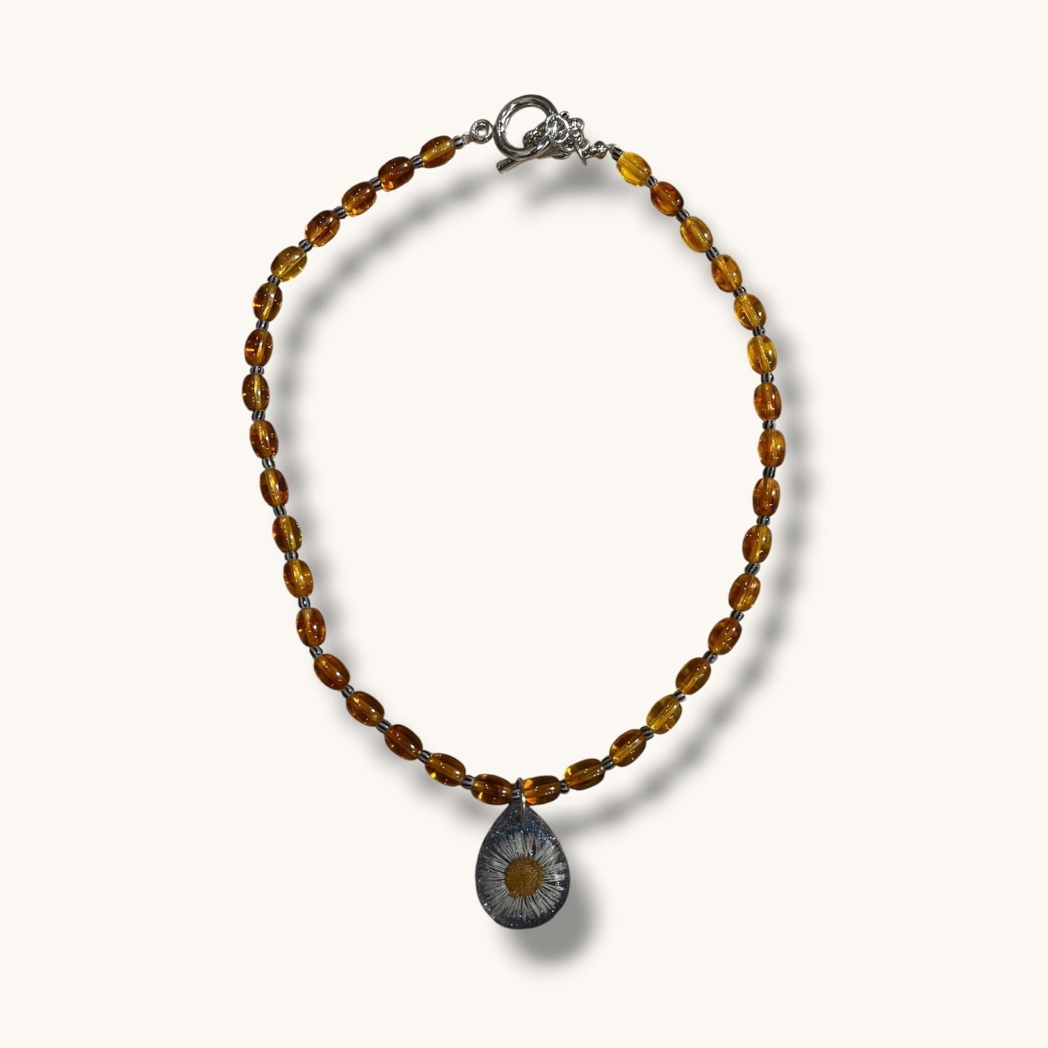 Teardrop resin pendant with a real white daisy flower on an amber beaded choker necklace with a silver toggle clasp